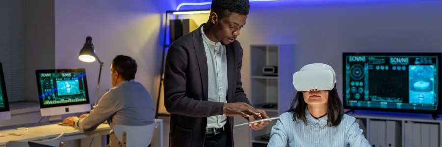 Office setting with a woman in a VR headset at a desk with sketches, accompanied by a man holding a tablet.
