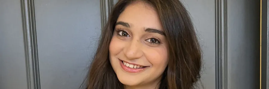 Disha Mehta smiling at the camera, her dark brown hair is long and wavy. It falls over her burgundy jacket.