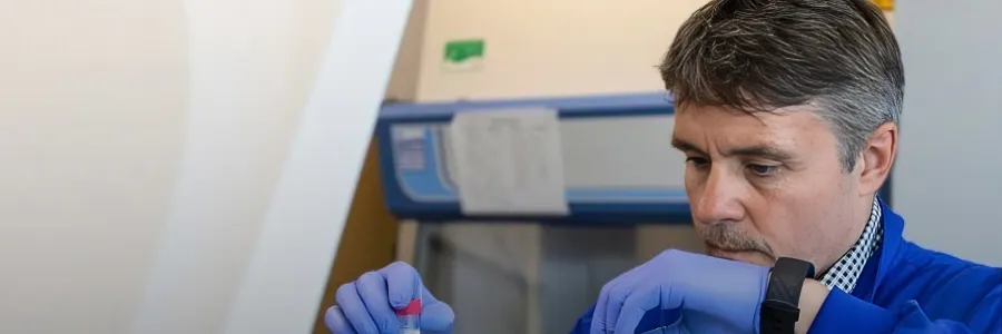 Professor Mark Cragg working in the lab. He is wearing a blue lab coat and holding two pipettes, one is each hand.