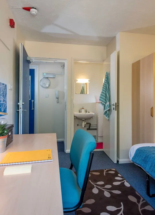 Student bedroom showing bed, desk and entrance to bathroom.