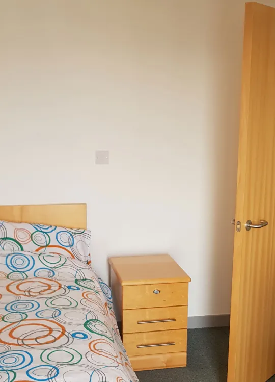 Bedroom with large double bed with floral sheets and a wooden nightstand.
