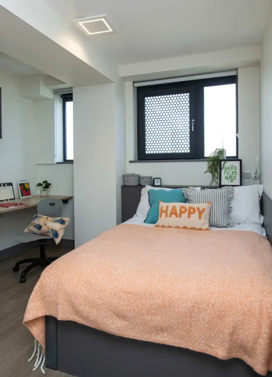 A standard bedroom showing a bed, a desk with shelves above and a chair.