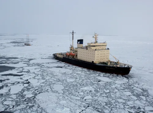 A ship surrouded by ice next to a small vassel.