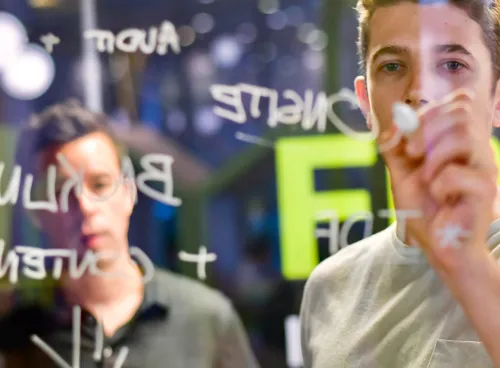 A man writing ideas on a glass wall with a marker pen