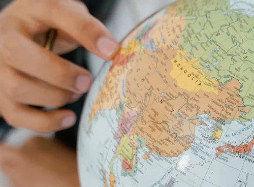 The hand of a young person points to a country on a globe model
