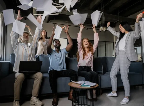 A diverse group of business people throw sheets of paper in the air
