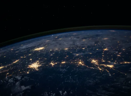 The darkened surface of the Earth at night, as seen from space, with lit-up cities visible.