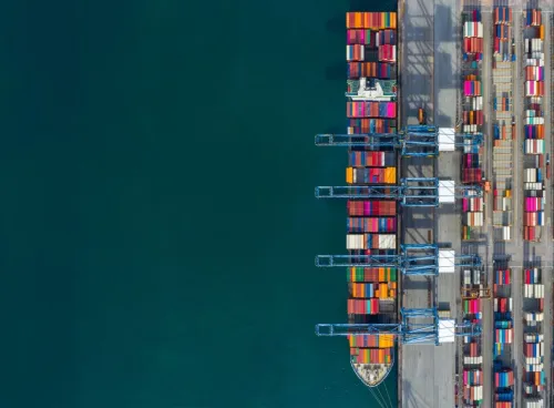 Top-down view of colourful shipping containers at a seaport with clear water