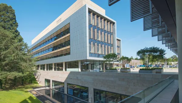 Exterior shot of modern building, surrounded by grass and trees, on a sunny day.