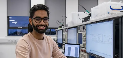 Student smiling to camera at electronics desk.
