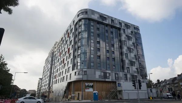 Tall, metal and glass apartment building surrounded by shops and roads.