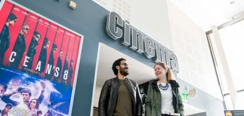 Two students walk underneath a sign reading "cinema". Movie posters adorn the walls.