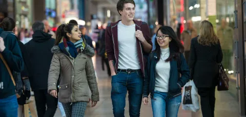 Group of students walking towards camera through a crowded shopping centre.