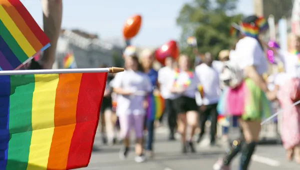 Pride flag with pride parade in the background.