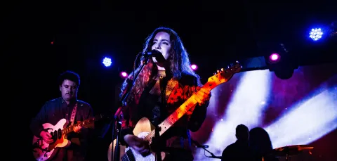 Female singer with guitar and band on small stage.