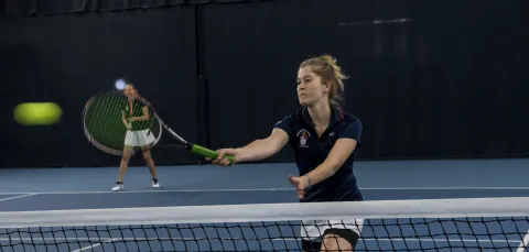 Student playing tennis in indoor sports hall. 