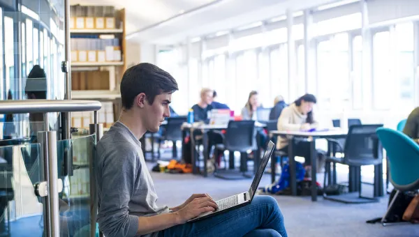 Student sitting with his laptop next to the windows in Waterfront Campus library.