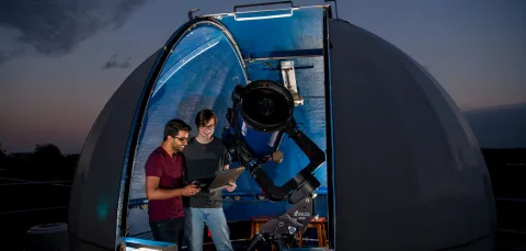 Astronomy students studying data in the shadow of a telescope and rooftop observatory dome.