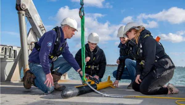 Several students at sea, crouching around an autonomous marine drone.