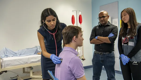 A medicine student uses a stethoscope on a patient while 2 other students watch