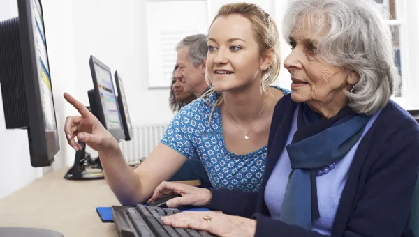 Several students sitting in pairs with elderly people, working together at computers.