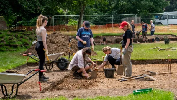 Archaeology students working at an excavation site with wheelbarrows and spades