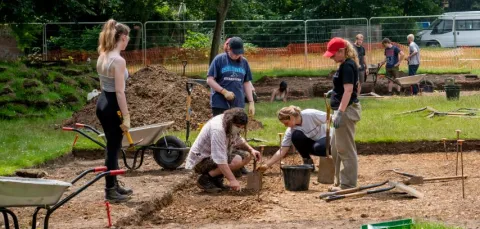 Archaeology students working at an excavation site with wheelbarrows and spades