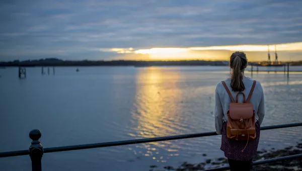 A student gazing reflectively over Southampton docks as the sun sets over the horizon in the distance.