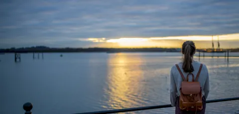 A student gazing reflectively over Southampton docks as the sun sets over the horizon in the distance.