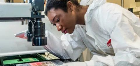 A researcher leaning over to observe the contents of a slide under a powerful microscope.