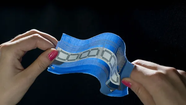 Two hands holding a piece of fabric with embedded circuitry