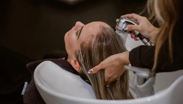 A hairdresser washes a client's hair at a basin