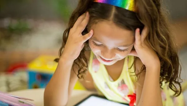 A young girl studies a tablet screen at a table