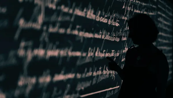 Stock image of a researcher's silhouette set against a wall projection of written language.