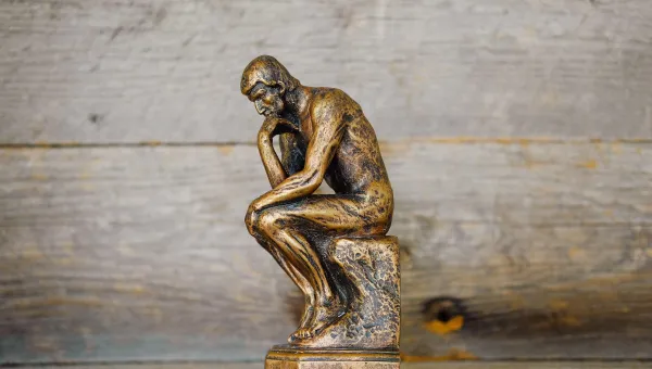 A small replica of 'The Thinker' - a bronze sculpture by Auguste Rodin depicting a man hunched over on a rock in contemplation - set against a backdrop of wood panels.