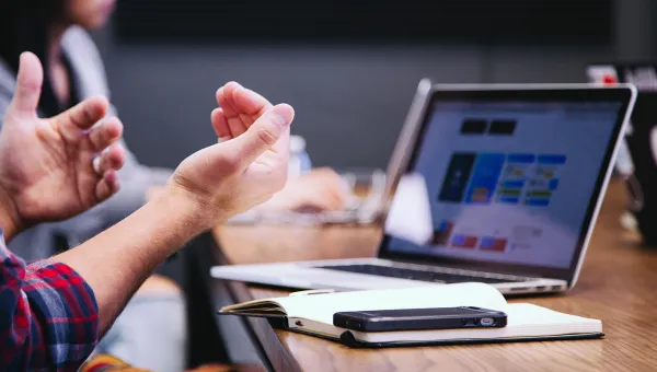 Laptop on a table with notepad and phone, user's hands in foreground 