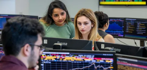 Students sitting at a desk, looking at desktop screens.