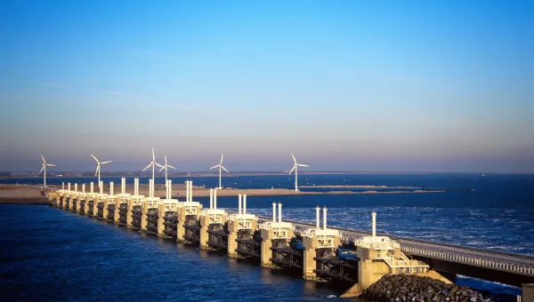 A wide shot of a storm surge barrier, with several wind turbines spinning in the background.