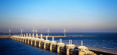 A wide shot of a storm surge barrier, with several wind turbines spinning in the background.