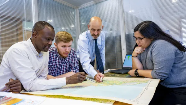 A Southampton Geospatial researcher points to a map as he stands over colleagues from the team