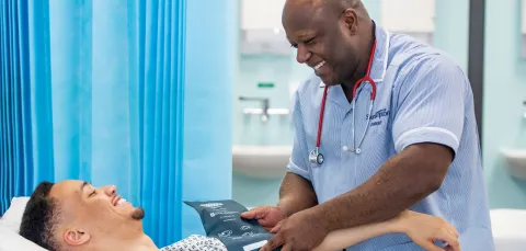 A patient and Southampton student nurse smiling at each other in a hospital room, as the nurse takes the patient's blood pressure.