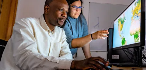 Two researchers stare intently at a screen with geographic information, one pointing to a specific area