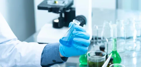 a lab bench with glass equipment and a hand holding a flask with coloured liquid