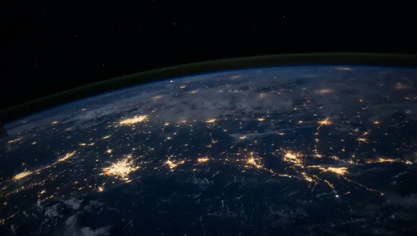 The darkened surface of the Earth at night, as seen from space, with lit-up cities visible.