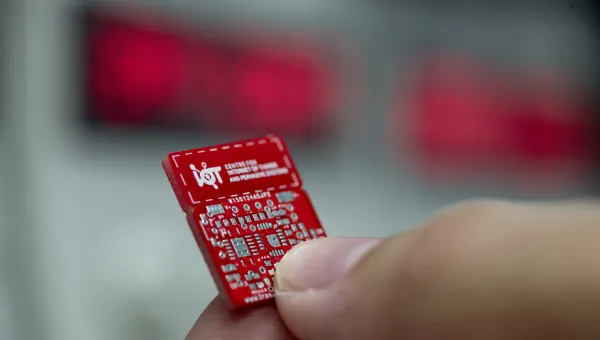Extreme close up of a red internet of things circuit board held between finger and thumb