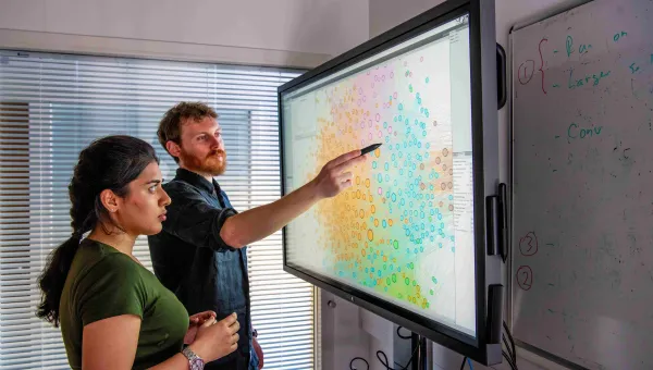 Two researchers looking at a multi-coloured plot on a large interactive screen