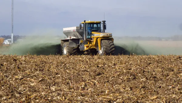 A tractor scattering crushed rock as it drives across a field.