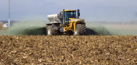 A tractor scattering crushed rock as it drives across a field.