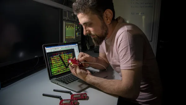Bearded young researcher examines a circuit board while sitting at a desk