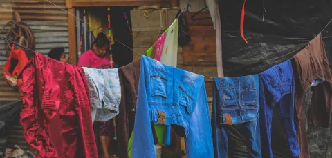 Woman walking past numerous people sitting along a fence covered in laundry